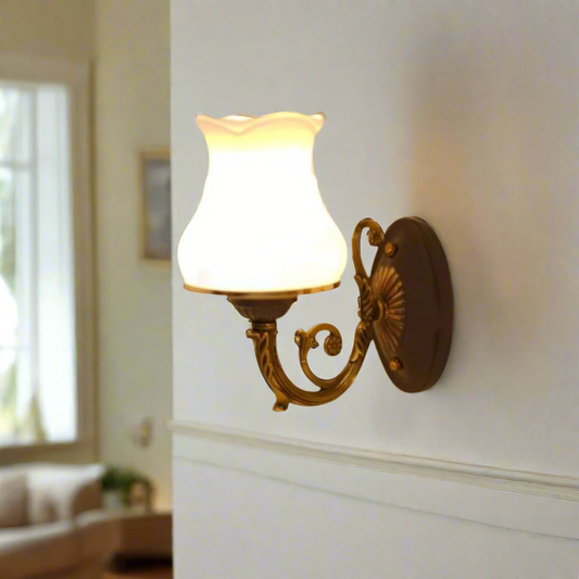 A brass wall sconce with a curved arm and a white fluted glass shade, blending modern and traditional elements.